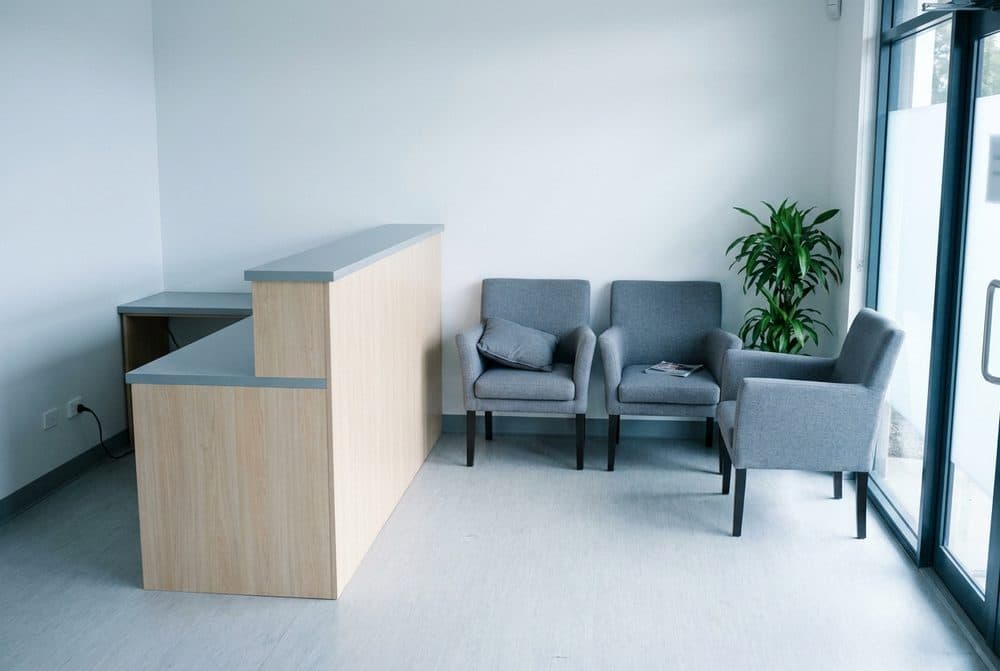 Recepção de clínica de fisioterapia com balcão de madeira clara e poltronas de espera