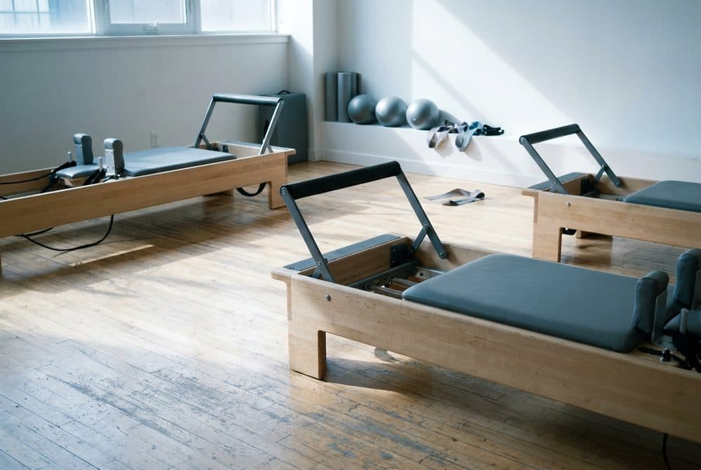Estúdio de Pilates com aparelhos reformer de madeira alinhados sobre piso de madeira